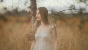 A serene portrait of a woman standing in a rural field, embracing nature.